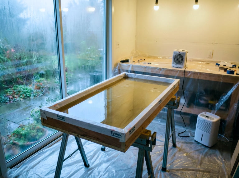 Nem kontrolü için plastik örtü, ısıtıcı ve nem alma cihazı bulunan nemli bir ev atölyesinde epoksi projesinin kürlenmesi.